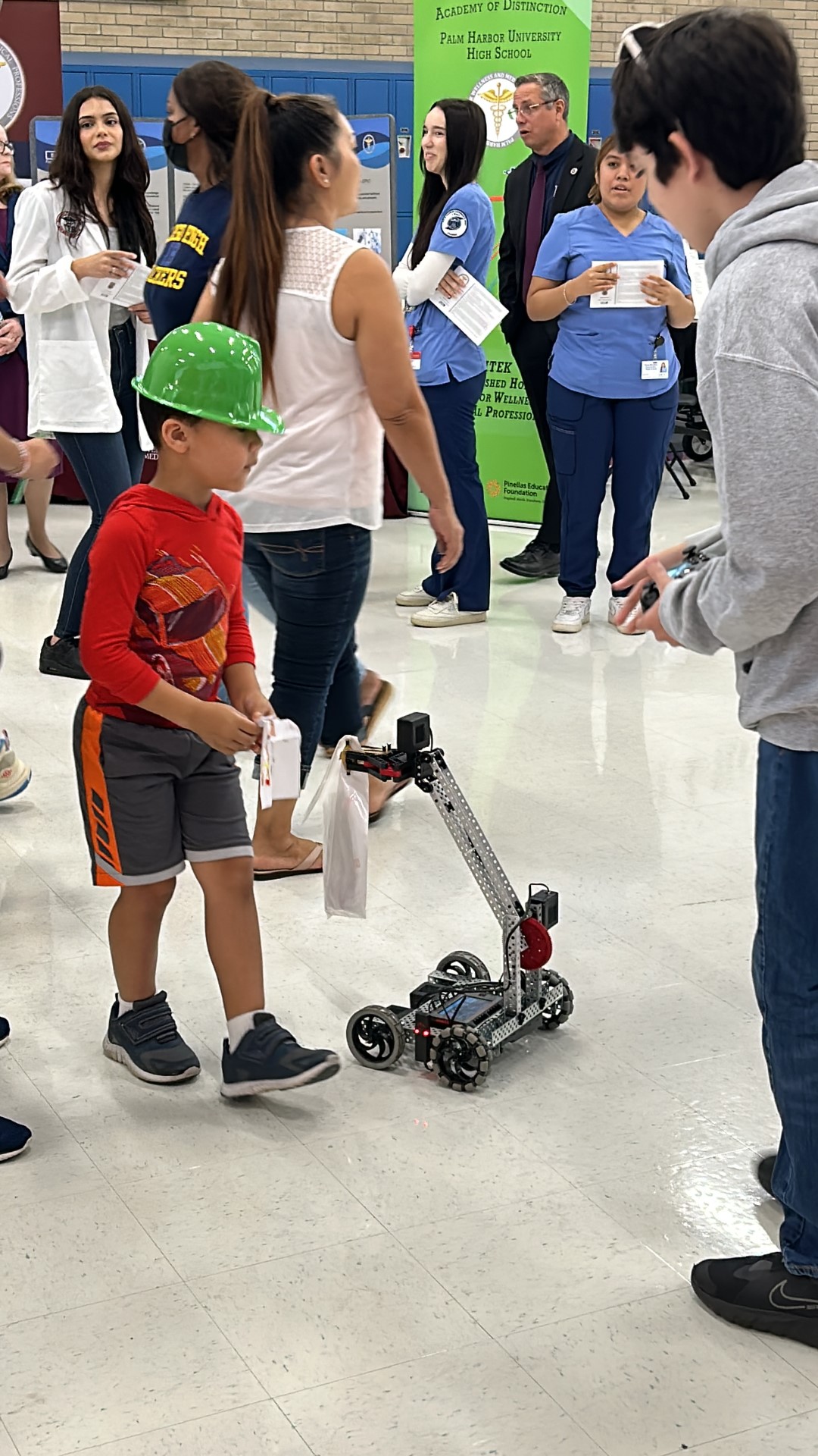 A child in a green hat standing next to a small robotDescription automatically generated